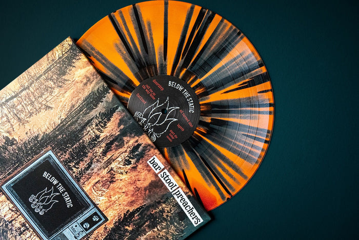 A vinyl LP with an Orange & Oxblood splatter design is partially pulled from its album cover, featuring earthy artwork and the text The Bar Stool Preachers and Below the Static—ideal for collectors or a standout album presale.