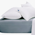 Two fluffy white pillows resting on a soft duck egg blue super king fitted sheet in a comfortable bedroom setting.