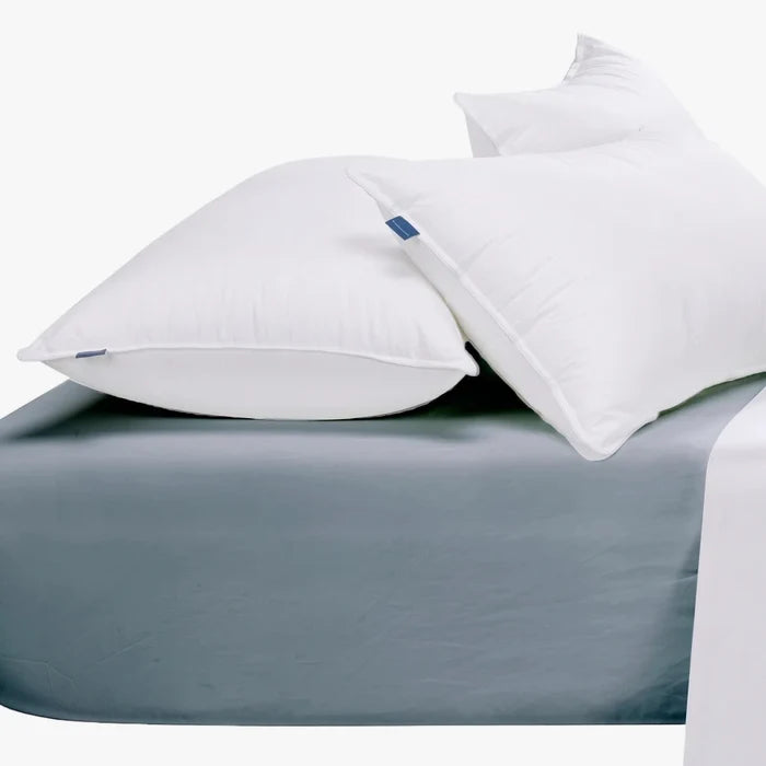 Two fluffy white pillows resting on a soft duck egg blue super king fitted sheet in a comfortable bedroom setting.