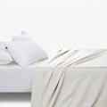 Cream cotton fitted sheet with two white pillows and a white fitted sheet on a bed, viewed from an elevated angle.