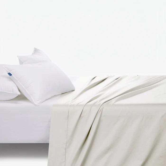 Cream cotton fitted sheet with two white pillows and a white fitted sheet on a bed, viewed from an elevated angle.