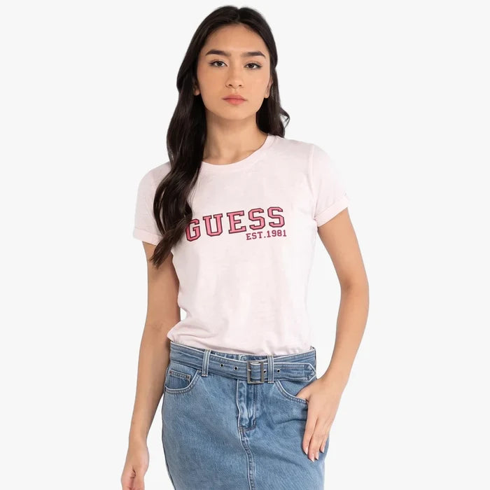 Front view of a woman wearing a pink Guess College short sleeve tee with the Guess logo, paired with a blue denim skirt.
