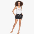Woman modeling Roxy New Impossible Love black shorts with a white tank top and sandals, full body shot.
