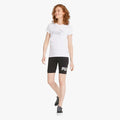 A smiling woman models a white Puma Ess+ Metallic Logo Short Sleeve Tee and black Puma cycling shorts, full body view.